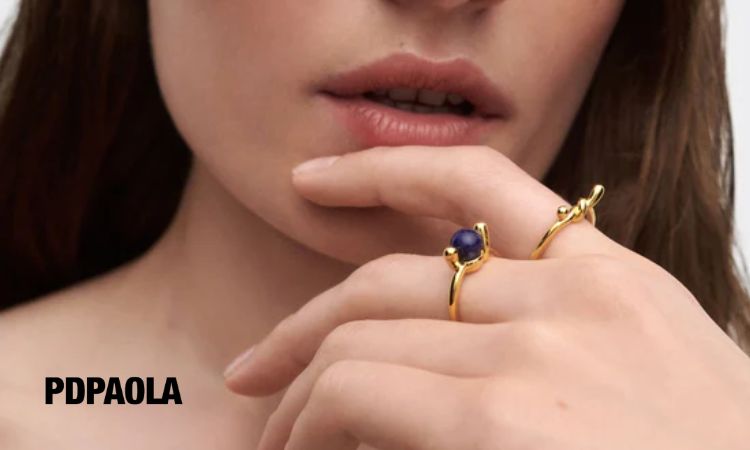 Fotografía detalle de la mano de una mujer junto a su barbilla. En sus dedos luce dos anillos de la marca PdPaola, que acaba de abrir su eCommerce en Chile.