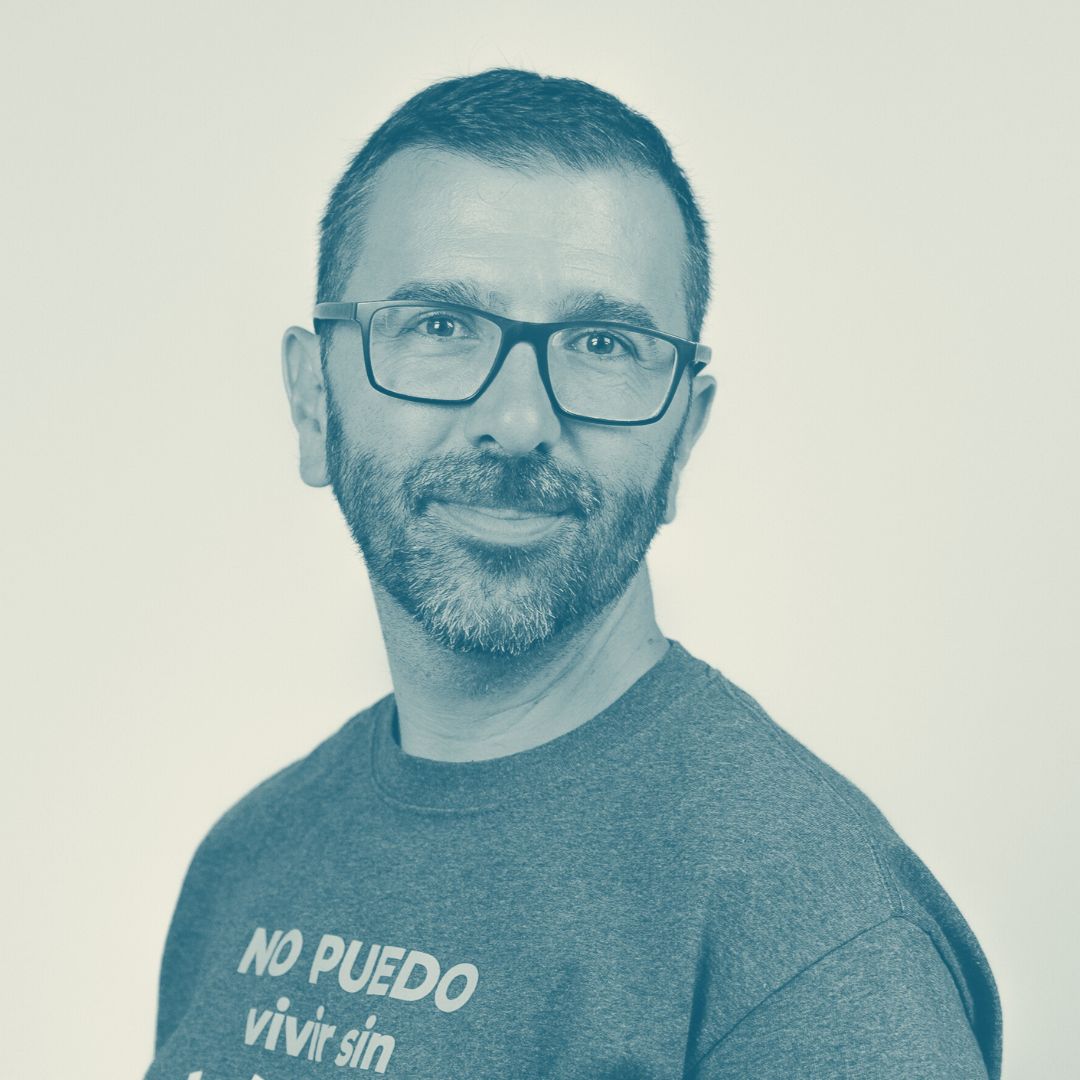 Un hombre con barba y gafas sonriendo en un fondo claro. Su camiseta dice: "NO PUEDO vivir sin podcasting". Fotografía de retrato amigable.